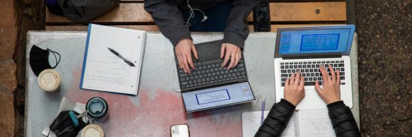 direct overhead view of two students typing on their laptops at a table 