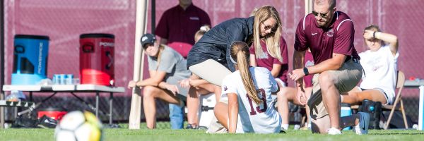 two trainers talking to and helping a soccer player who is on the ground