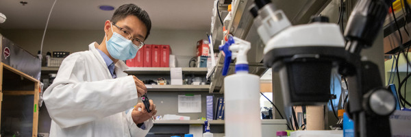 person in lab coat and mask working with equipment in a laboratory