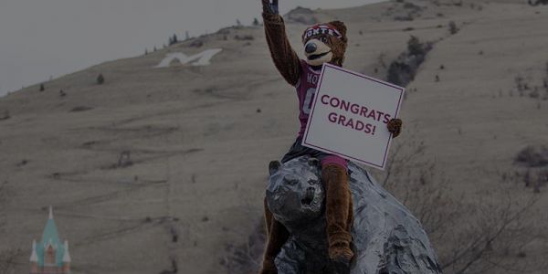 Picture of Monte on Grizzly statue holding a sign that reads 'Congrats Grads'