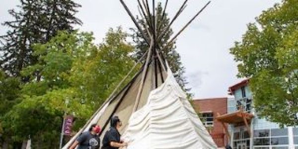 Three students erect a teepee in front of the Native American Center