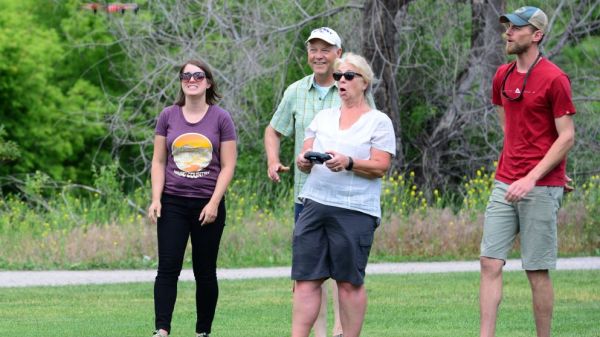 woman holding a controller while the drone hovers in front of her, with a group of onlookers