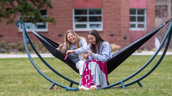 Two female students laugh while sitting in a hammock on the University of Montana Oval.