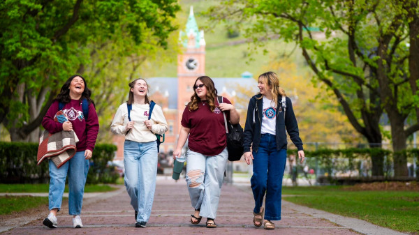 A group of four young women walks side by side on a picturesque brick path, sharing laughter and conversation.