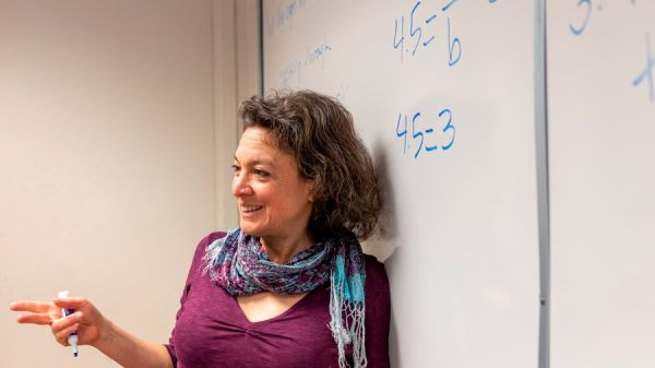 Woman in a pink dress standing in front of a white board with math on it