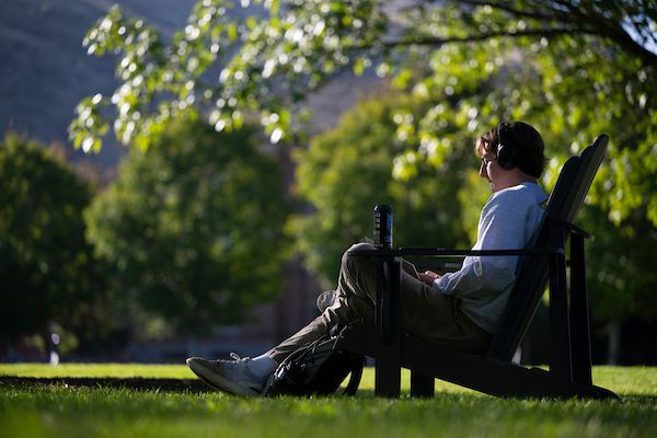 student sitting outside listening to music on headphone on the UM campus