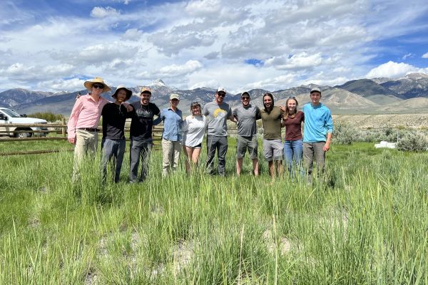 OCRMW members stand in a green field underneath a cloudy sky, arms wrapped around each other convivially.