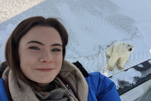 Dr. Stephanie Penk smiling with a polar bear below them in the distance
