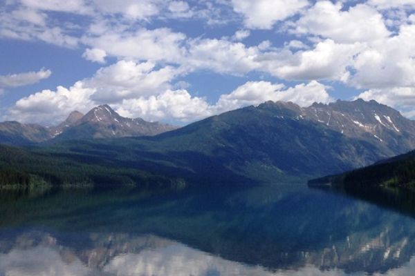 row of mountains reflected in a lake below a cloudy blue sky