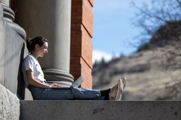 Student sitting outside using a computer, working on their laptop in an outdoor campus space.