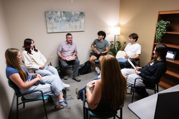 A male counselor sits in a circle with a variety of UM students, engaged in a free group therapy session