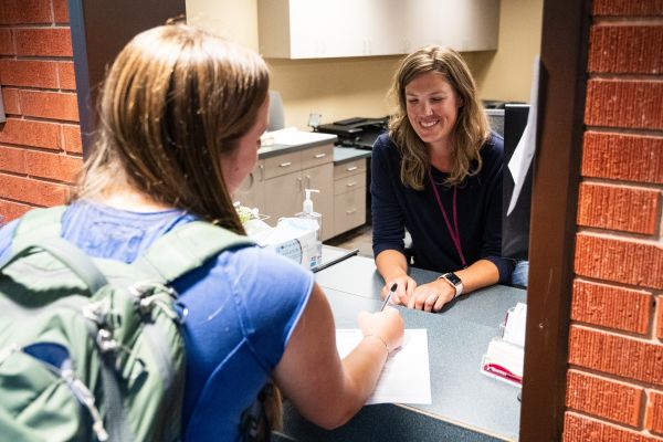 Student checking in at medical reception desk, speaking with front desk staff at Curry Health Center.