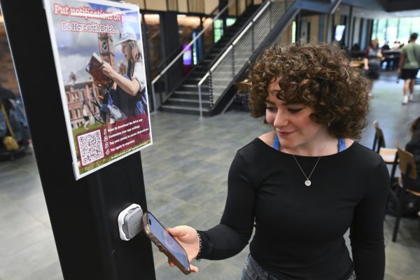 A student uses her phone at a Brick station inside the Lodge Dining Center, demonstrating how the Brick device helps reduce digital distractions and support focused, present engagement on campus.