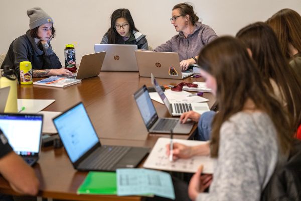 group of individuals sitting at a table with laptops open in collaboration