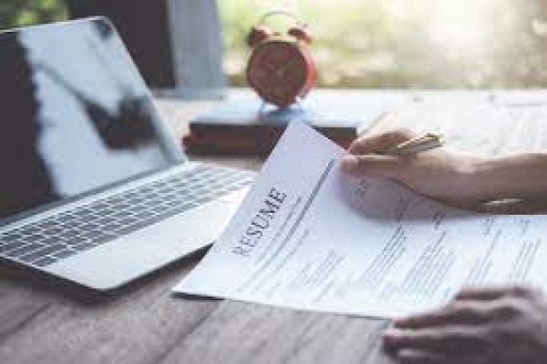 close up view of hands holding a resume in front of an open laptop