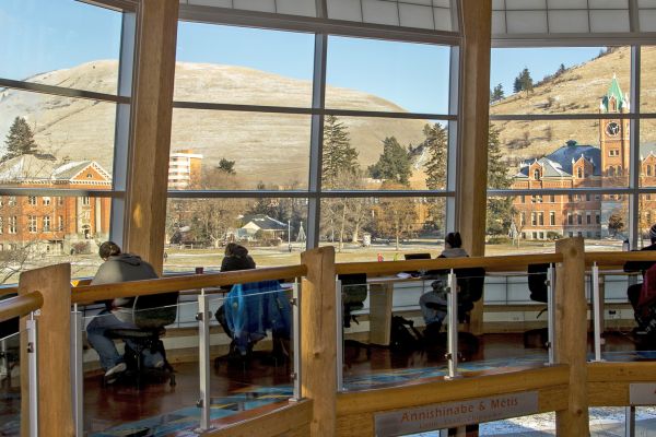 row of large windows with students working on a table along them in the PFNAC