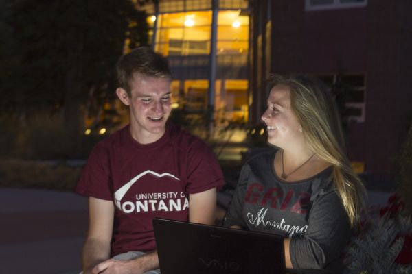 Two students smiling at night while working on the Oval