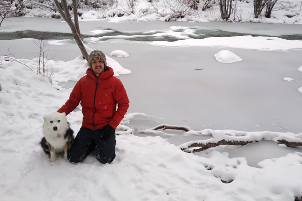 Zachary Lauffenberger posing with dog in front of snowy creek