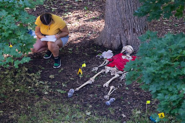 student leans over skeleton in forest