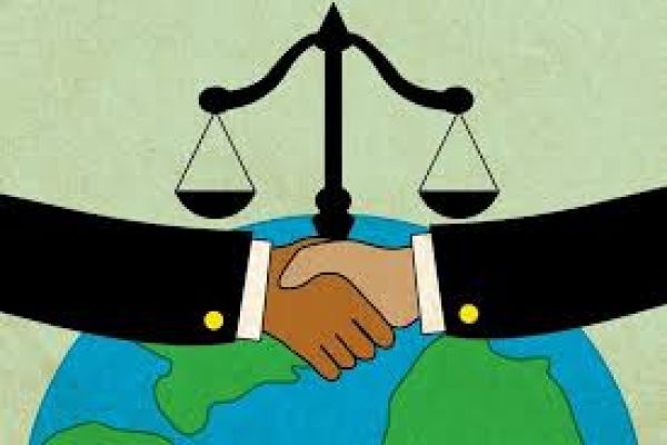 two hands shake in front of globe and justice scales