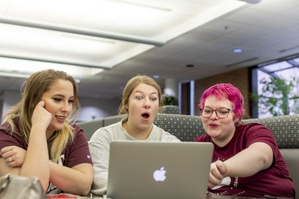 Three students using a laptop looking surprised