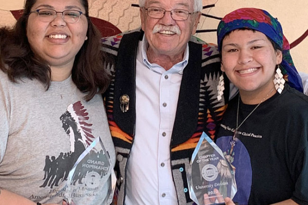 Past members of AIBL holding trophy's from a nations business idea competitions next to the advisor of the club