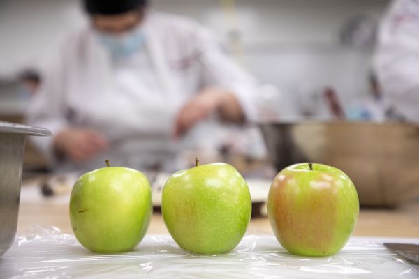 Three green apples in foreground with culinary student in background