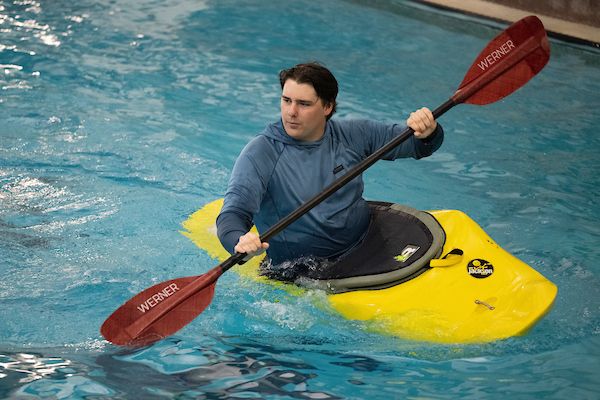 A student learns to kayak in the swimming pool.