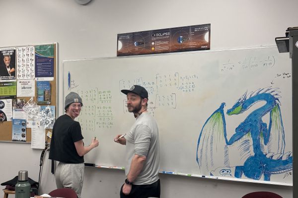 two students write equations on a white board