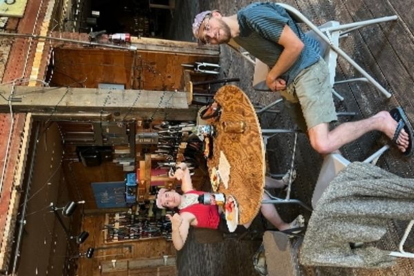 Two adults around a table, looking at the camera, one with thumbs up