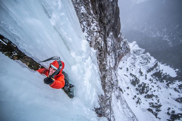 person climbing up sheet of ice with ice axe