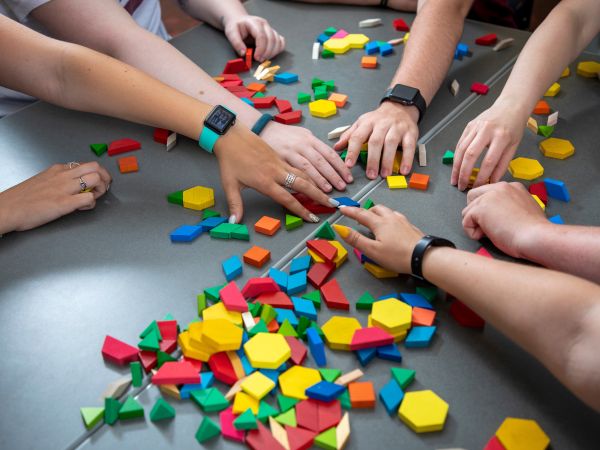Several hands reaching for colored blocks on a table