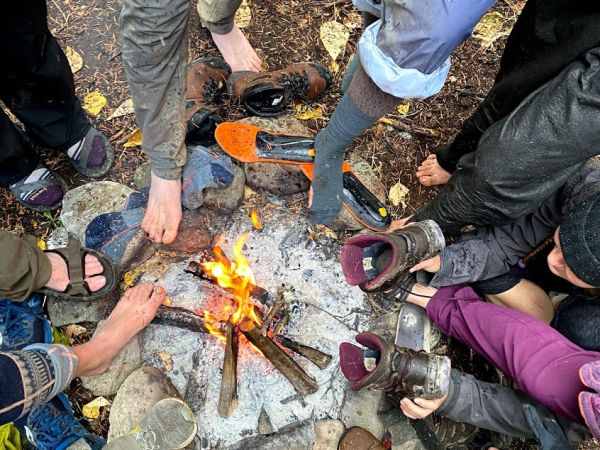 Students warm their feet and dry their boots around a campfire