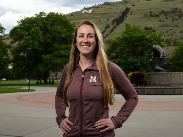 Anna smiles for a portrait wearing University of Montana apparel in front of the Grizzly Bear Statue at UM
