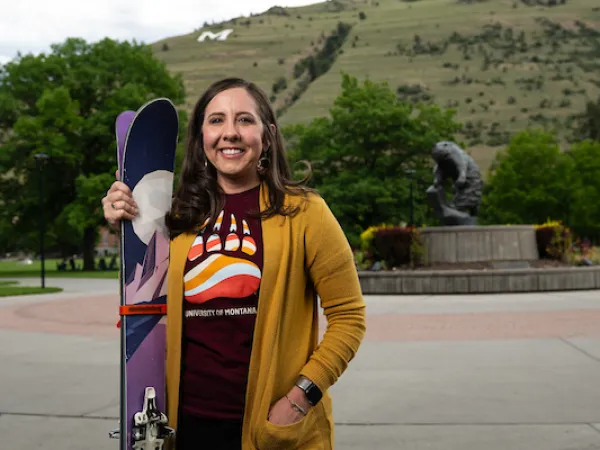 Julie Ann Williams stands her skis next to her and smiles for a portrait wearing University of Montana apparel in front of the grizzly bear statue