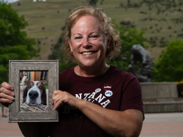 Kate smiles for a portrait and is holding a framed portrait of a dog