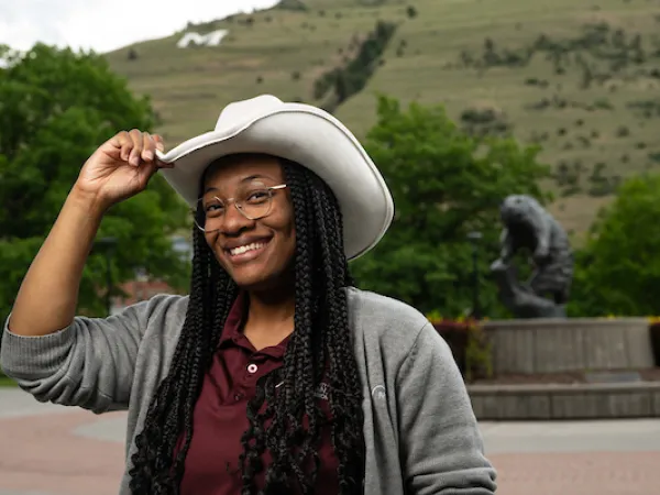 Zen smiles for a portrait while wearing a cowboy hat and UM apparel in front of the Grizzly bear statue