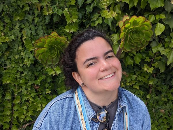 Mary Venegas smiles in front of a wall of succulents 