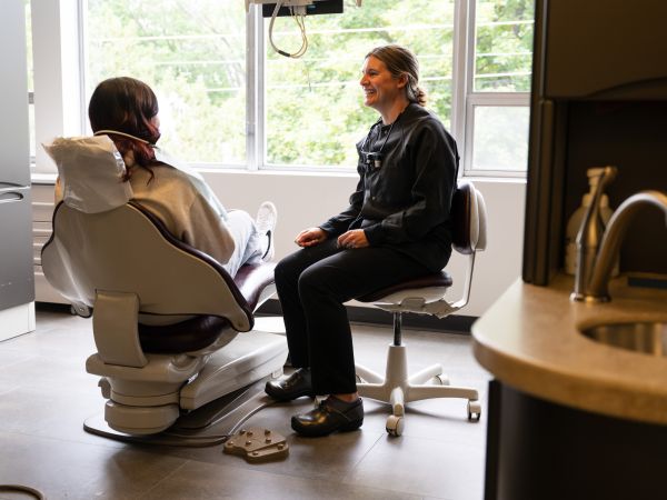 A student sits in a Dental chair next to the Curry Health Center Dentist. Both are smiling, engaged in conversation.