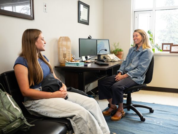 A psychiatric nurse practitioner speaking with a student during a clinical consultation in an office setting.
