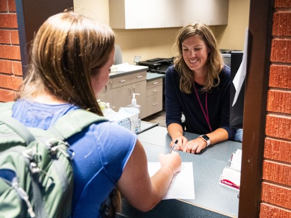 Student checking in at medical reception desk, speaking with front desk staff at Curry Health Center.
