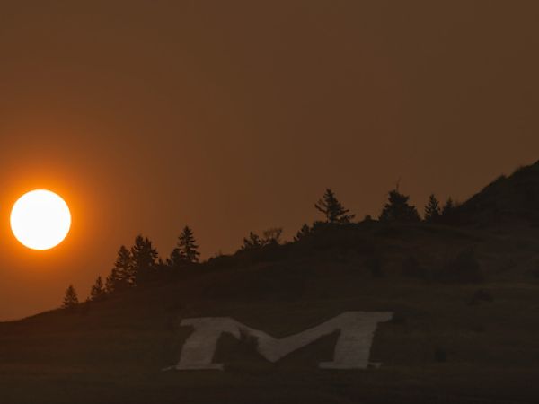 The M hill with smoke in the background and a red sun
