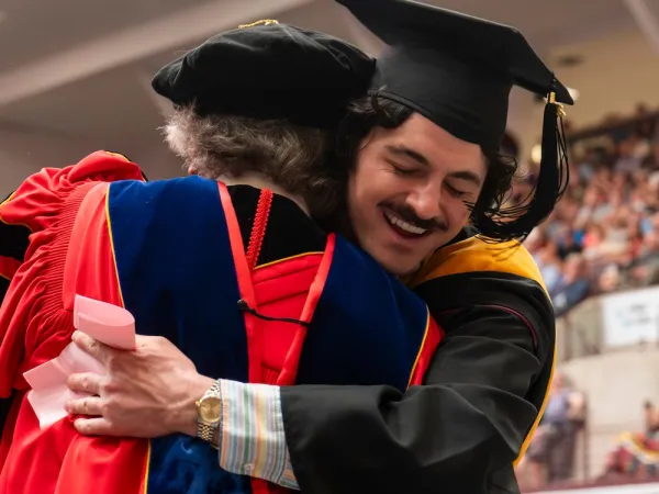 A UM graduate embraces a faculty member on the stage at Commencement
