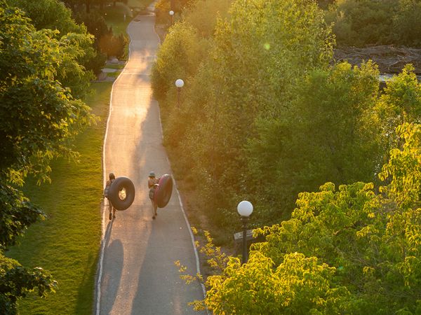 Two students walk the river trail carrying inner tubes