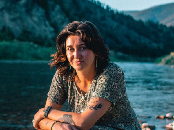 woman squats on a rock near the river and looks at the camera unsmiling