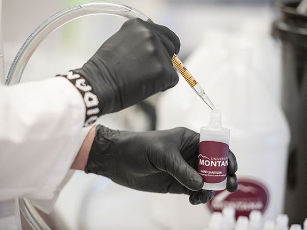 Gloved hands fill a bottle of Griz hand sanitizer.