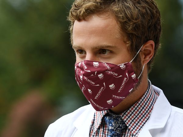 A student with a white medical coat on and a UM facemask