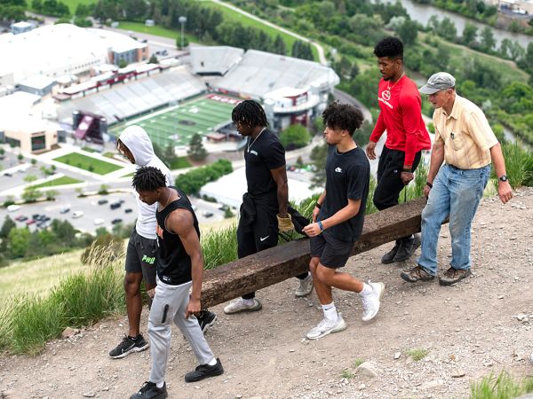 M Trail project leader Dr. Steve Gaskill carries a railroad tie with Griz football players earlier this summer.
