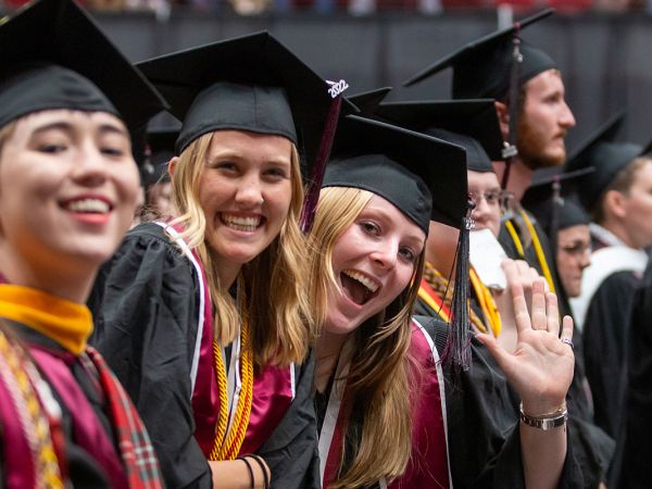 Female students smile and wave at graduation.