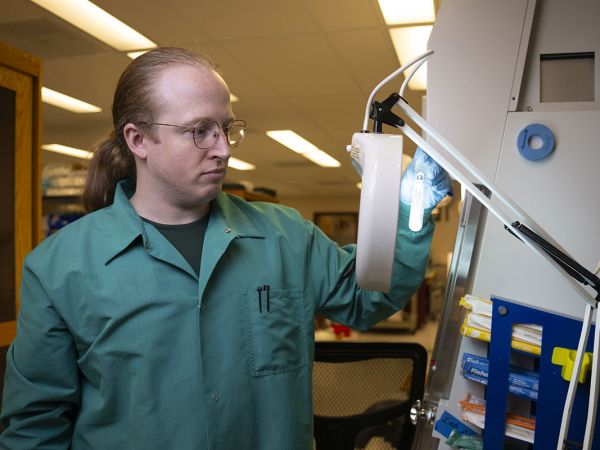 Research associate Alexander Riffey holds up a glowing test tube.